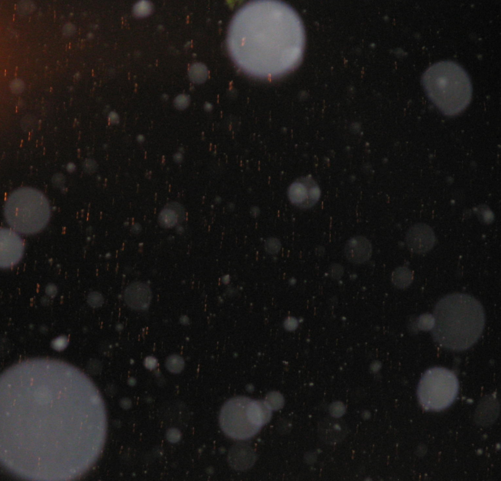 Night sky with out-of-focus white bokeh circles and orange rain streaks across the darkness.